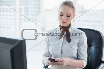 Blonde serious businesswoman using smartphone