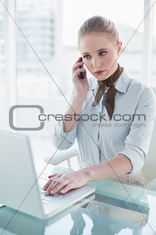 Blonde serious businesswoman using laptop and phoning
