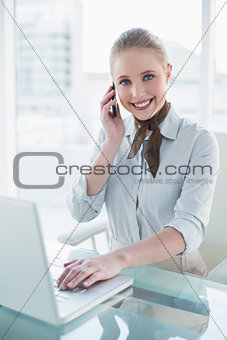 Blonde smiling businesswoman using laptop and phoning