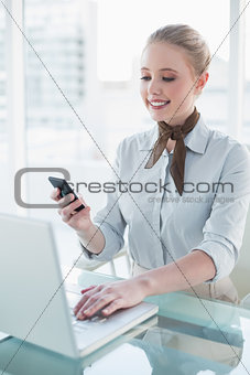 Blonde smiling businesswoman using laptop and smartphone