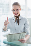 Blonde cheerful businesswoman holding newspaper and showing thumb up