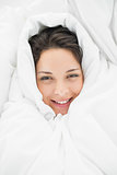 Smiling casual brunette wrapped up in her duvet