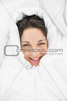 Smiling casual brunette wrapped up in her duvet