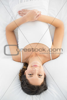 Pleased casual brunette in white pajamas lying on her bed