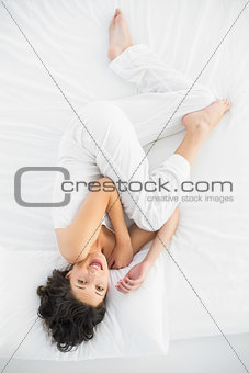Cheerful casual brunette in white pajamas lying on her bed and making funny faces