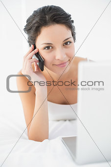 Content casual brunette in white pajamas making a phone call