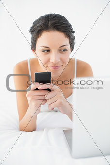Peaceful casual brunette in white pajamas using her mobile phone