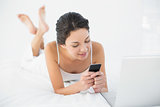 Calm casual brunette in white pajamas using her mobile phone