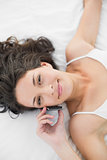 Peaceful casual brunette in white pajamas calling with her mobile phone