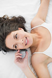 Cheerful casual brunette in white pajamas calling with her mobile phone