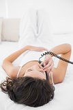 Peaceful casual brunette in white pajamas calling with a telephone