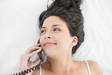Happy casual brunette in white pajamas calling with a telephone