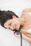 Joyful casual brunette in white pajamas calling with a telephone