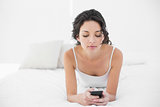 Relaxed casual brunette in white pajamas texting with a mobile phone