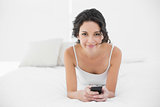 Cheerful casual brunette in white pajamas texting with a mobile phone