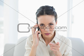 Irritated stylish brunette businesswoman making a phone call and pointing camera with her finger