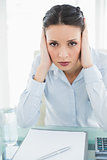 Upset stylish brunette businesswoman holding her head and looking at camera
