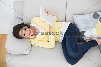 Joyful casual brunette in yellow cardigan using a tablet pc