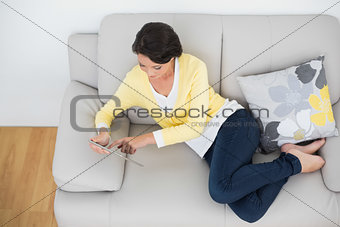 Relaxed casual brunette in yellow cardigan using a tablet pc