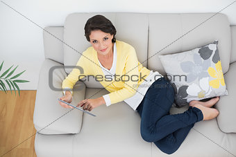 Amused casual brunette in yellow cardigan using a tablet pc