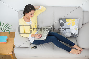 Relaxed casual brunette in yellow cardigan typing on a laptop