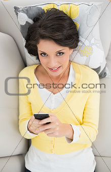 Happy casual brunette in yellow cardigan using a mobile phone