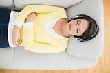 Peaceful casual brunette in yellow cardigan listening to music with headphones