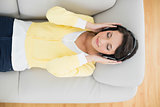 Calm casual brunette in yellow cardigan listening to music with headphones