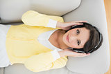 Smiling casual brunette in yellow cardigan listening to music with headphones