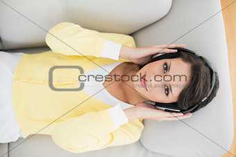 Smiling casual brunette in yellow cardigan listening to music with headphones