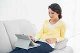 Content casual brunette in yellow cardigan using a tablet pc