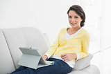 Smiling casual brunette in yellow cardigan using a tablet pc