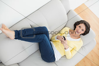 Relaxed casual brunette in yellow cardigan holding a mobile phone