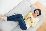 Relaxed casual brunette in yellow cardigan texting with a mobile phone