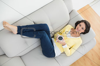Relaxed casual brunette in yellow cardigan holding a mug of coffee