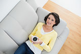Content casual brunette in yellow cardigan holding a mug of coffee