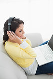 Content casual brunette in yellow cardigan listening to music while using a laptop