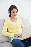 Pretty casual brunette in yellow cardigan listening to music while using a laptop