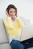 Happy casual brunette in yellow cardigan listening to music with headphones