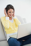 Relaxed casual brunette in yellow cardigan listening to music while using a laptop