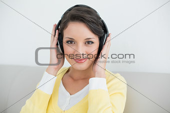 Content casual brunette in yellow cardigan listening to music with headphones