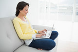 Beautiful casual brunette in yellow cardigan using a laptop