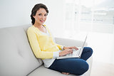 Attractive casual brunette in yellow cardigan using a laptop