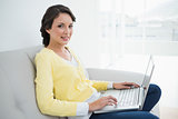 Charming casual brunette in yellow cardigan using a laptop