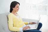 Charming casual brunette in yellow cardigan typing on a laptop