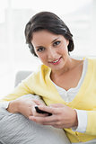 Happy casual brunette in yellow cardigan texting with a mobile phone