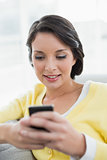 Concentrated casual brunette in yellow cardigan texting with her mobile phone