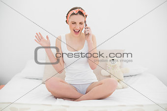 Phoning young woman sitting on her bed