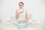 Sick woman holding a handkerchief sitting on her bed