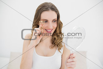 Woman using an eyelash curler while looking into a mirror
